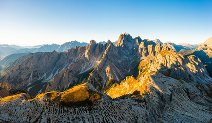 Edges of high peaks at sunrise. Illuminated by the rays of the sun, the craggy peaks of Tre Chime di Lavaredo under a clear sky aerial view in backlight - obrazy, fototapety, plakaty