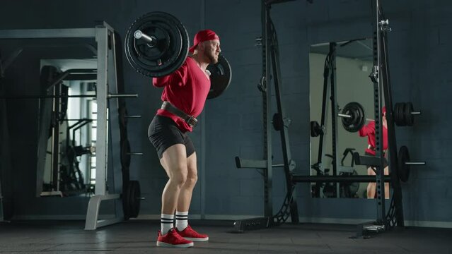 professional bodybuilder squats with a barbell in the gym, dressed in red clothes.slow motion 