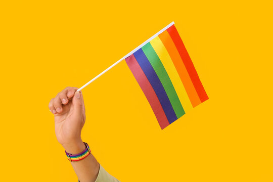 Young man with LGBT flag on yellow background
