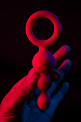 Woman holding anal beads in neon pink blue light. 