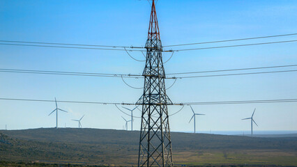 High voltage power line against rotating windmill wind turbines in valley. Concept of green...