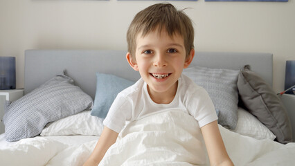 Boy lying in bed, opening his blanket and laughing at the camera, radiating a sense of fun and...