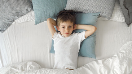 Cute little boy waking up in bed and stretching out hands