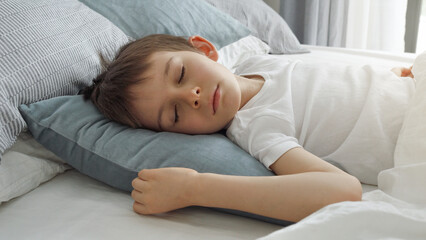Portrait of little boy sleeping in bed at morning. Modern bedroom with big window.