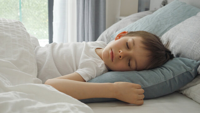 Closeup of little boy sleeping in bed next to window at morning. Kids resting, child healthcare and relaxation