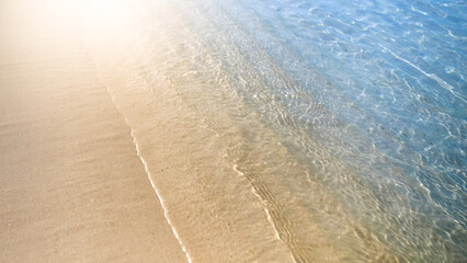 Slow motion of camera flying over calm sea waves rolling on sandy beach