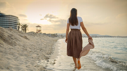 Woman enjoying her holiday on the sandy sea beach, walking with a silk scarf. Concepts of travel, journey, and tourism.