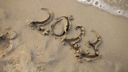 Closeup of female finger writing 2023 year on sea beach next to rolling waves