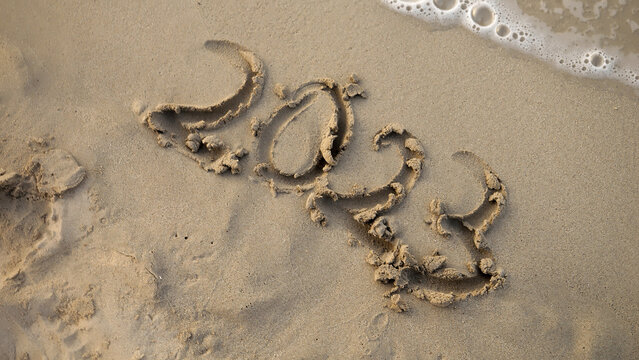 Closeup of female finger writing 2023 year on sea beach next to rolling waves