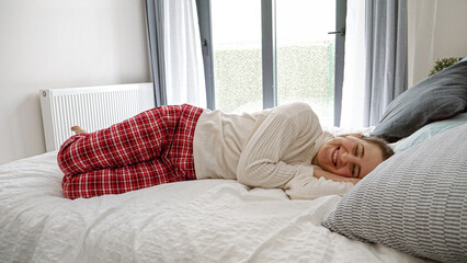 Cheerful woman in pajamas lying on the bed and laughing with delight. Concept of happiness, joy, and carefree attitude at home.
