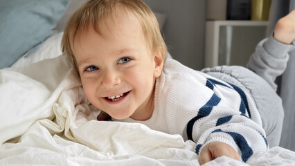Cute smiling baby boy with blond hair and blue eyes lying in bed and smiling in camera