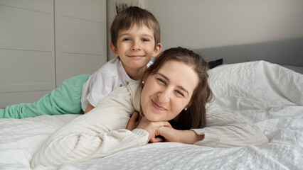 Portrait of cheerful smiling boy with mother in pajamas lying in bed and having good time together