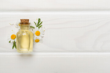 Bottle with chamomile essential oil and flowers on wooden background, top view
