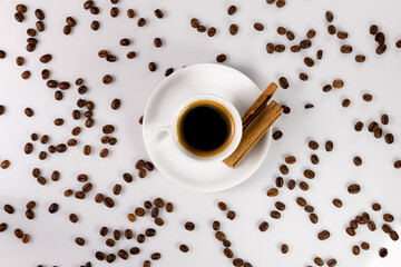 Café negro con ramas de canela, con granos de café en vista cenital, sobre fondo blanco