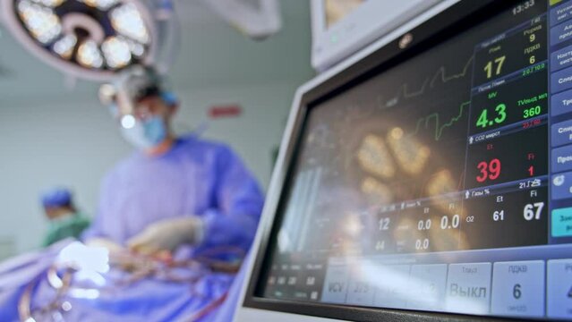 Patient's life signs during the surgery on the monitor of equipment. Doctors work at backdrop in blur.