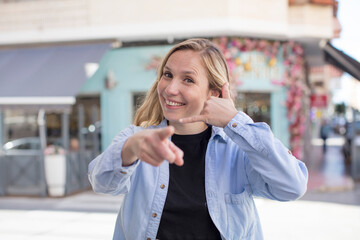 pretty woman smiling cheerfully and pointing to camera while making a call you later gesture, talking on phone