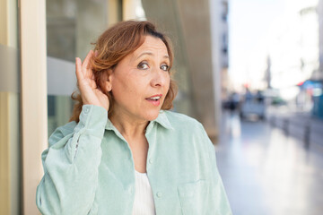middle age woman looking happy, listening, trying to hear a secret conversation or gossip,...