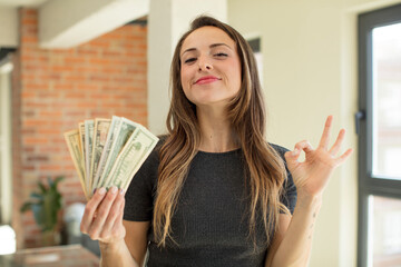 pretty woman feeling happy, showing approval with okay gesture. dollar banknotes concept