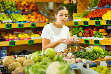 Focused young woman shopper chooses ripe watermelon radish at grocery supermarket