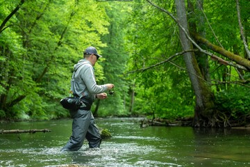 Fisherman crossing river with spinning rod in his hands. Trout fishing.