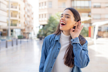 pretty young adult woman looking happy, listening, trying to hear a secret conversation or gossip,...