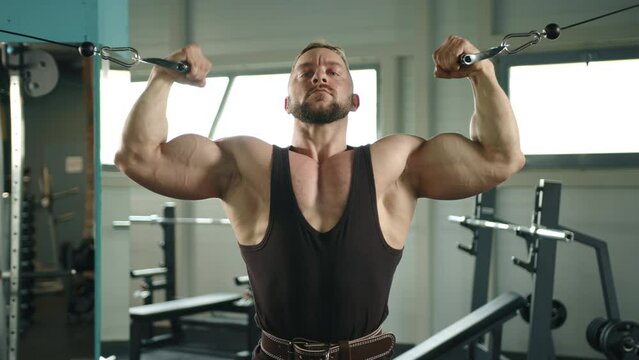 muscular athlete pumps biceps in the crossover mashine . looking at the camera. slow motion. High quality 4k footage