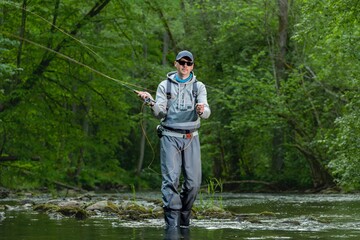 Fisherman catching brown trout on the fly standing in river.