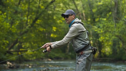 Fototapeta premium Fisherman catching brown trout on spinning tackle standing in river.