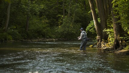 Fototapeta na wymiar Fisherman catching brown trout on spinning tackle standing in river.