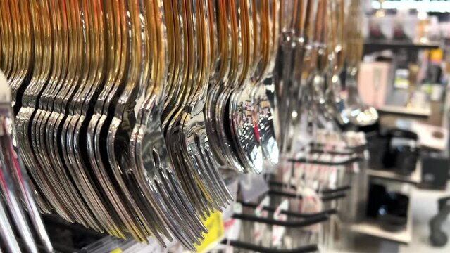 New expensive cutlery - spoons and forks hanging on the counter in the crockery store or tableware shop. Close-up
