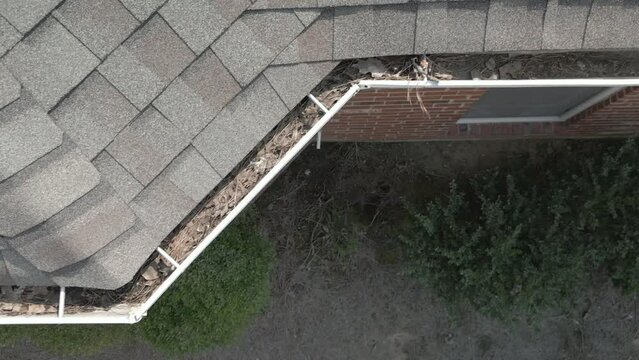 Dirty, metal gutters on a residential home are clogged with leaves and debris.