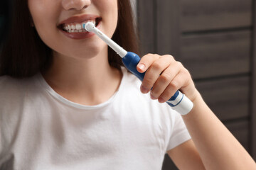 Woman brushing her teeth with electric toothbrush in bathroom, closeup