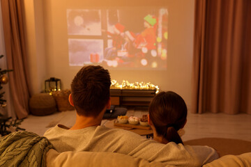 Couple watching Christmas movie via video projector in cosy room, back view. Winter holidays...