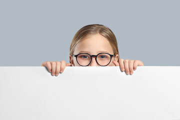 Cute girl looking out of placard on light grey background. Space for text