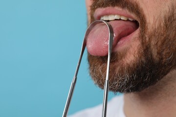 Man brushing his tongue with cleaner on light blue background, closeup. Space for text - obrazy, fototapety, plakaty