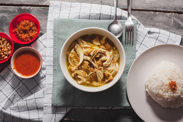 Soto Ayam is a authentic recipe from Indonesia especially Java. Served with cabbage, boiled egg, and chilli sauce. Top view on white bowl. Soto ayam is a kind of chicken soup with a yellowish sauce.