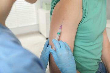 Doctor giving hepatitis vaccine to patient in clinic, closeup