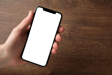 Woman holding smartphone with blank screen at wooden table, top view. Mockup for design