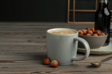 Mug of delicious coffee with hazelnut syrup on wooden table, space for text