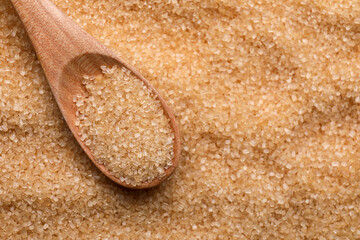 Brown granulated sugar and wooden spoon as background, closeup