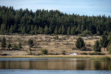 View of Laguna Zeta, with a hill with pine trees and a motorhome on the shore, in Esquel, Chubut,...