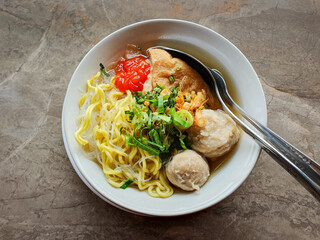 Tofu meatballs with noodles and sauce and celery leaves in a bowl.