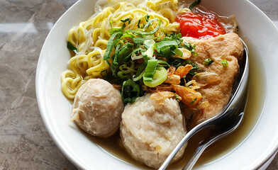 Tofu meatballs with noodles and sauce and celery leaves in a bowl.