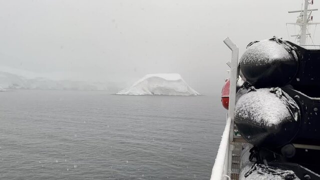 Static view onboard expedition ship at Melchior Islands in Antarctic Peninsula. Heavy snowfall with poor visibility. Ship&acute;s lifeboat and zodiacs partially visible and radar scanners rotating.