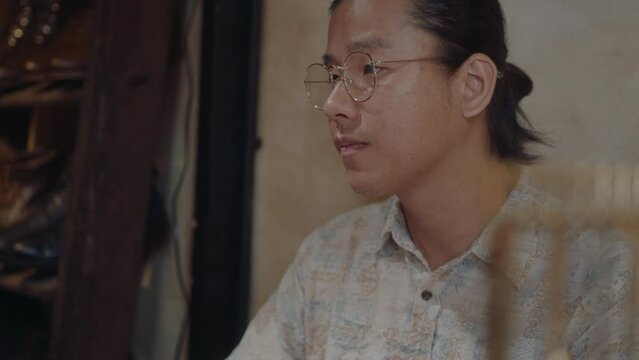 Young Asian man working on computer in pawn shop or antiques store. Medium close-up shot