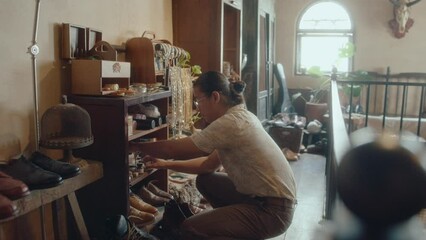 Asian man cleaning up the shelf in consignment store, checking shoe restoration products, working with antiques collection