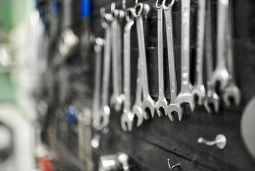 Wrenches and other hardware hanging on a tool board in a bicycle repair shop. Close up view with selective focus.