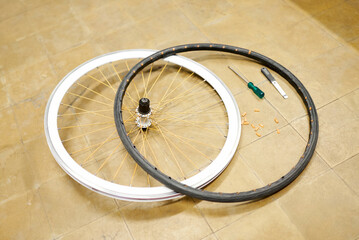 Bicycle wheel and airless tire disassembled on the floor of a bike repair shop. White rim, orange spokes, black tire.