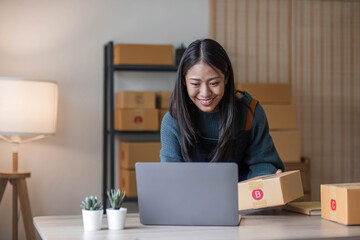 Young beautiful happy asian business woman owner of SME online using laptop receive order from...