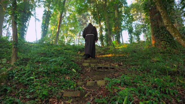Fraile franciscano monje religioso católico, cristiano meditando y rezando caminando por el sendero contemplando la naturaleza en el bosque al amanecer subiendo escalera de piedra